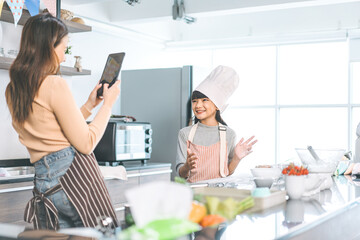 Happy asian family mother and daughter cooking in kitchen selfie with smartphone for social media