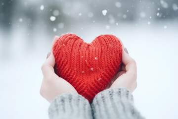 Fototapeta premium Female hands holding a red knitted heart in snow
