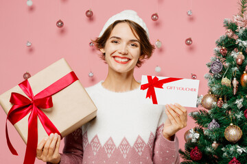 Merry young woman wear white sweater hat posing hold present box gift certificate coupon voucher...