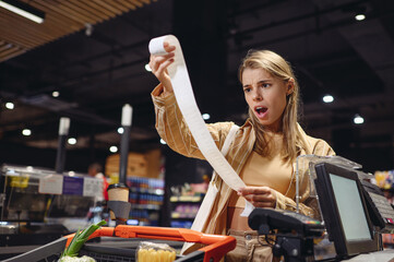 Young sad customer woman wear casual clothes read bill at checkout shopping at supermaket store...