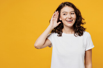 Young curious nosy smiling cheerful Caucasian woman wear white blank t-shirt casual clothes try to hear you overhear listening intently isolated on plain yellow orange background. Lifestyle concept.