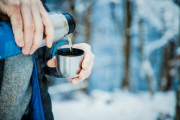 man pouring hot tea in winter forest