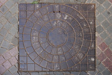Rusty circular iron manhole cover on the sidewalk. Circular metal plate covering road water drainage