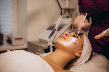 Cosmetologist applying mask on woman's face in beauty salon.
