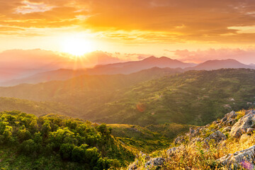 highland mountain landscape of beautiful sunset or sunrise with nice mountain peaks and slopes, green and golden hills and majestic cloudy sky on background