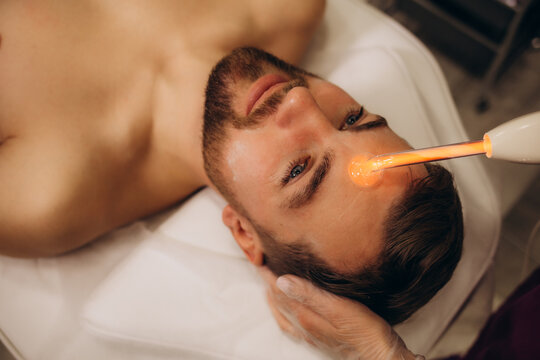 Skin treatment with darsonval device. Young caucasian man, beauty clinic. Stimulating collagen production.