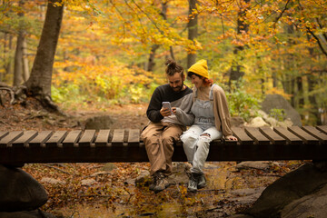 Fototapeta premium male and female couple talking on the phone, taking selfie in the forest with sitting on a bridge