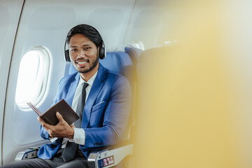 Young businessman sitting in airplane using laptop and smart phone