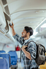 Male tourist traveling by plane Passengers place their carry-on luggage in lockers above their...