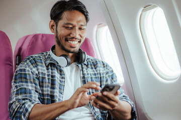 Male tourist using a mobile phone while on the plane