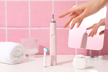 Electric toothbrush, glass, mirror, towel and hand on pink background