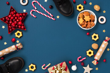 Christmas card with children's shoes, sweets, candy, gingerbread cookies, gifts on blue background, top view.   Saint Nicholas Day, 6 December.