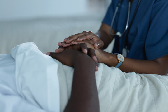 African american female doctors and male patient is lying in bed holding hands in hospital room
