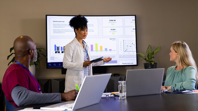 Happy diverse female foctor with tablet giving presentation to colleagues at office meeting