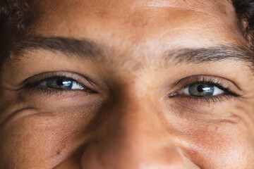Eyes of happy biracial man with long dark curly hair laughing in sunny living room at home