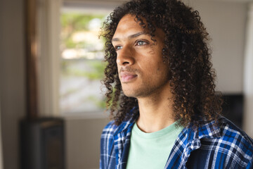 Pensive biracial man with long curly hair looking ahead in sunny living room at home
