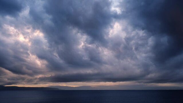 Real time dramatic sunrise at the beach. Dark tropical storm clouds with colourful lights moving against the sky. Magnificent nature landscape. First rays of the sun above the sea on a windy morning.