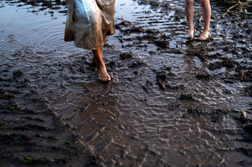 A mother and child wade barefoot through a muddy field, only dirty feet
