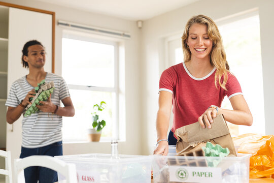Happy diverse couple sorting rubbish for recycling in sunny kitchen at home - Powered by Adobe