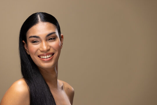 Fototapeta Portrait of biracial woman with dark hair, smiling and natural make up on brown background