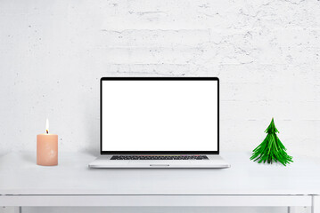 Laptop mockup on desk with Christmas decor, tree, and calendar. Cozy holiday office scene for...