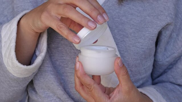 Woman opening white jar of wrinkle moisturizer or wrinkle cream, hands with jar of cream 
