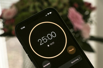 A phone with a black and orange 25-minute timer to study with the pomodoro method on a blurry...