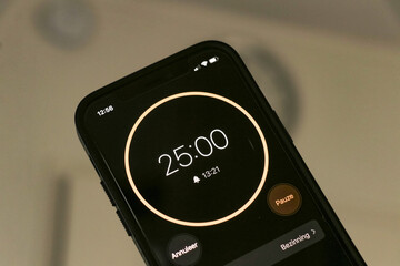 A phone with a black and orange 25-minute timer to study with the pomodoro method on a blurry background