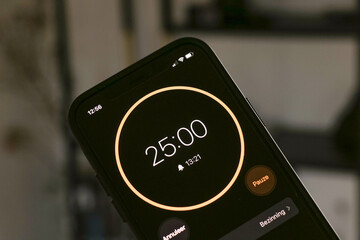 A phone with a black and orange 25-minute timer to study with the pomodoro method on a blurry background