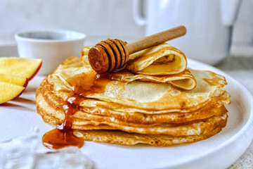 A stack of pancakes with honey on a white ceramic plate. Pancakes with honey and nectarines on a light background. Pancakes on a white plate, selective focus. Russian traditions. Russian holiday. Masl