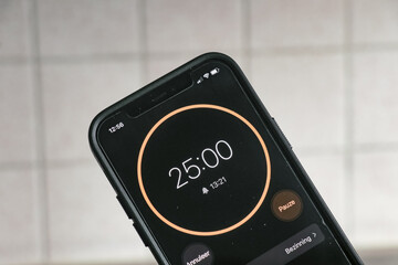 A phone with a black and orange 25-minute timer to study with the pomodoro method on a blurry...