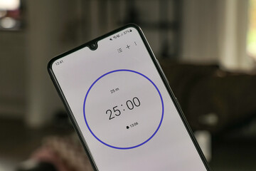 A phone with a white 25-minute timer to study with the pomodoro method on a blurry livingroom background