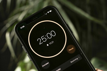 A phone with a black and orange 25-minute timer to study with the pomodoro method on a blurry...