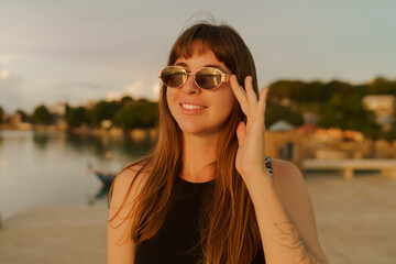 Beautiful brunette woman with stylish hairstyle walking outdoor   on the pier. Warm  sunser colors.  Travel and vacation concept.