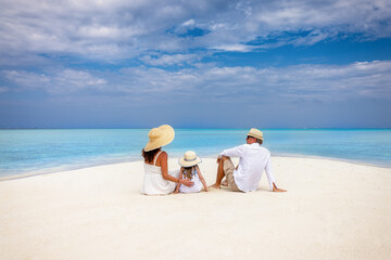 A beautiful family in white summer clothing relaxes on a tropical paradise beach with turquoise sea in the Indian Ocean