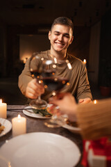 Cheerful happy couple in love drinking wine and having romantic dinner at home or restaurant. Home date and clinking wine glasses.