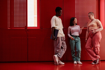 Diverse group of gen Z young people standing against red metal wall in futuristic office space