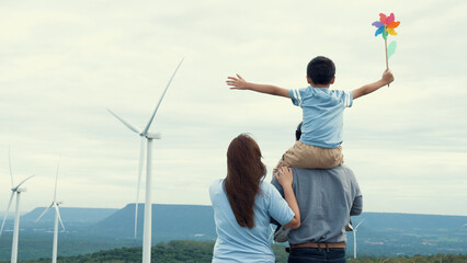 Concept of progressive happy family enjoying their time at the wind turbine farm. Electric generator from wind by wind turbine generator on the country side with hill and mountain on the horizon. © InfiniteFlow