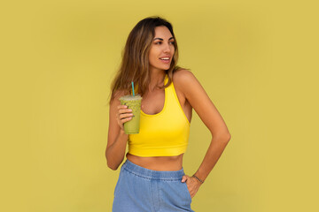 Studio photo of pretty brunette woman in sportive outfit  hoding beverage and posing on yellow background. Perfect slim body.