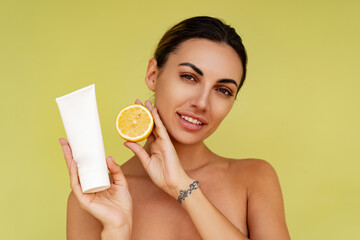 Beautiful woman holds tube with cosmetic cream and lemon. Photo of attractive woman with perfect makeup on  yellow  background. Beauty concept