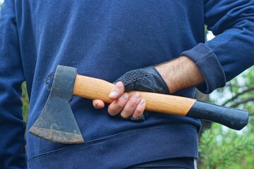 one  small new  classic  sharp hatchet with a wooden handle for chopping wood is held in his hand...