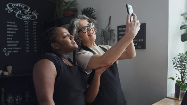 Medium shot of Caucasian elderly and African American co-workers standing in coffee house taking selfies