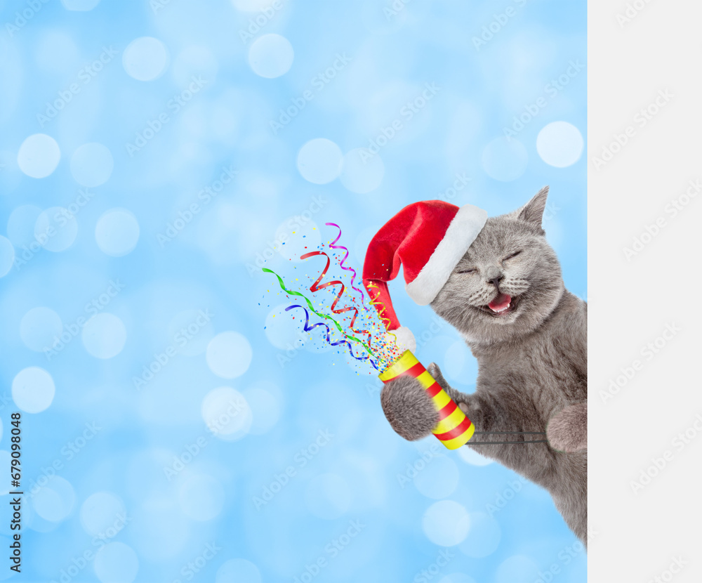 Aufkleber Happy cat wearing red santa hat holds exploding firecracker and looks from behind empty white banner on festive blue background
