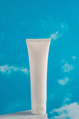Plastic white tube for cream or lotion. Skin care or sunscreen cosmetic on blue sky background.