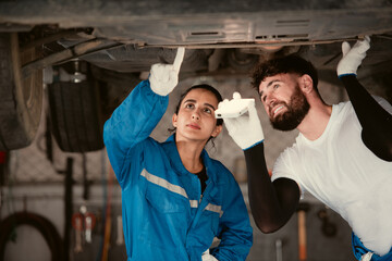 Bothe of car mechanic working in an auto repair shop, Check the operation of the engine of under the car that comes in for repairs at the auto repair shop.