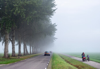 traffic on bicycle and car to school and work during morning mist in the netherlands near utrecht - obrazy, fototapety, plakaty