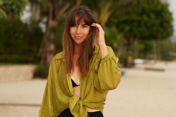 Fototapeta premium Attractive brunette woman in stylish casual summer outfit posing on the tropical beach during vacations.