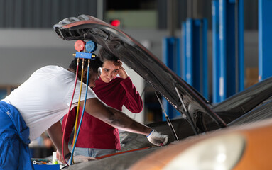 Car mechanic working in an auto repair shop explain to customer after inspecting the operation of the car's air conditioner and refrigerant