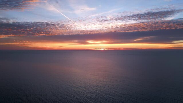 A view from a drone flying over the sea early in the morning at sunrise, with the rising sun and a colorful sky