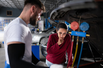 Car mechanic working in an auto repair shop explain to customer after inspecting the operation of...